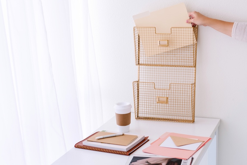 Woman putting paperwork in gold wire vertical tray - a tip on how to declutter fast.