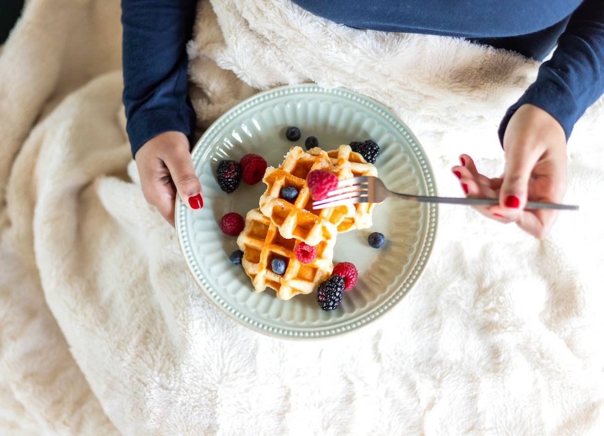 Woman eating waffles in bed - self care routine ideas.