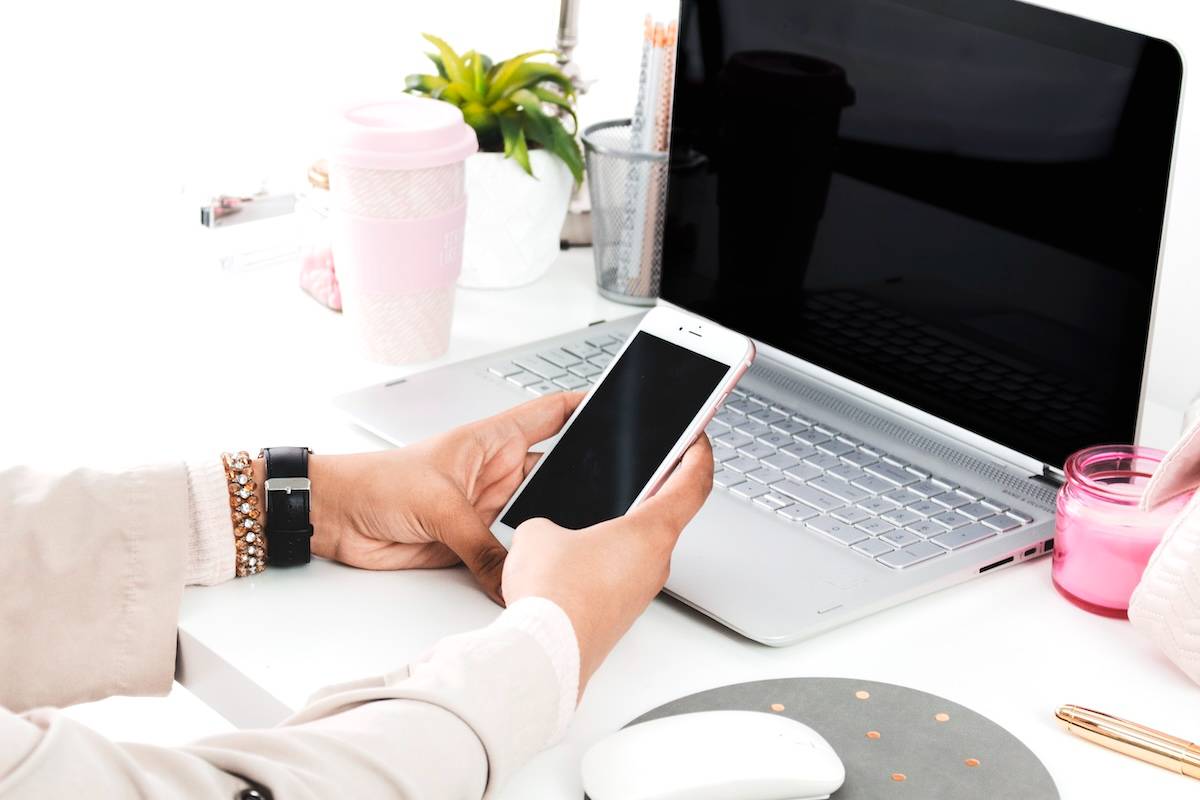 Woman holding phone in front of laptop - items you need to be organised.