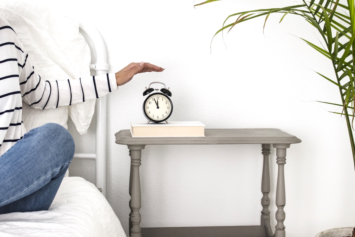 Woman on bed hitting an alarm clock - tips for a bedroom declutter.