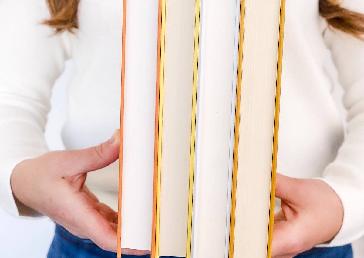 Woman holding 4 books - book decluttering guide.